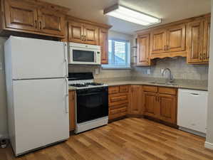 Kitchen featuring white appliances, brown cabinetry, light stone counters, and decorative backsplash