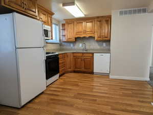 Kitchen with white appliances, brown cabinetry, open shelves, light wood-type flooring, and backsplash