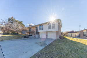 Bi-level home with brick siding, a front yard, a garage, driveway, and a chimney