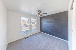 Carpeted empty room featuring wooden walls, a ceiling fan, and an accent wall
