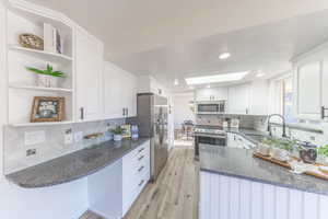 Kitchen with a skylight, dark stone countertops, white cabinets, stainless steel appliances, and light wood-style floors