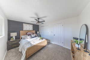 Bedroom with carpet flooring, ceiling fan, an accent wall, multiple closets, and wood walls