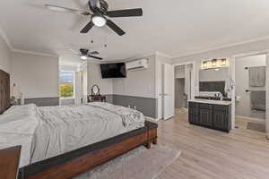 Bedroom featuring ensuite bathroom, ornamental molding, ceiling fan, light wood finished floors, and a wall unit AC