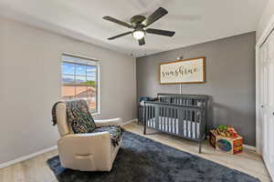 Bedroom with a crib, ceiling fan, light wood finished floors, and a closet
