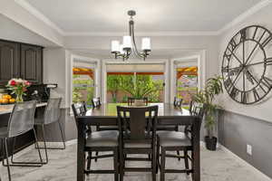 Dining space featuring plenty of natural light, crown molding, light marble finish flooring, and a chandelier