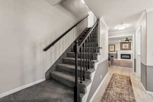Stairway with a glass covered fireplace, ceiling fan, ornamental molding, and wood finished floors