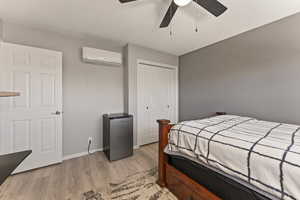 Bedroom featuring light wood-type flooring, a ceiling fan, a closet, and a wall unit AC