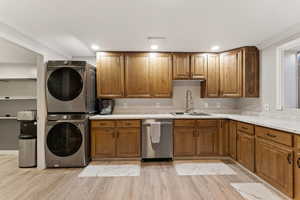 Kitchen featuring brown cabinets, stainless steel dishwasher, light wood finished floors, stacked washer / drying machine, and crown molding