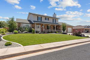 Traditional-style house with a porch, brick siding, a front lawn, and a chimney
