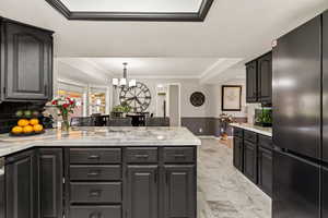 Kitchen with freestanding refrigerator, crown molding, light stone countertops, a peninsula, and pendant lighting