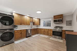 Kitchen featuring stainless steel appliances, brown cabinetry, stacked washer and clothes dryer, and electric panel