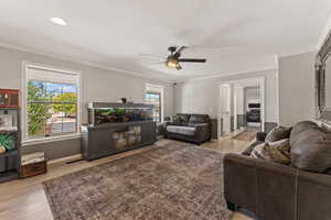 Living room featuring a ceiling fan, light wood finished floors, and crown molding