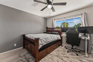 Bedroom with a ceiling fan, light wood-style floors, and a desk