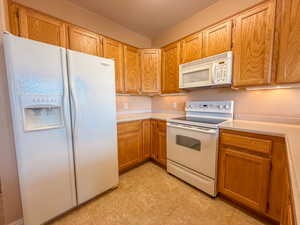 Kitchen featuring white appliances, light countertops, and brown cabinets