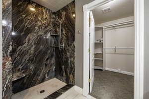 Bathroom with a spacious closet, a marble finish shower, and light colored carpet