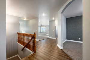 Corridor featuring an upstairs landing, an accent wall, dark wood finished floors, and a textured ceiling
