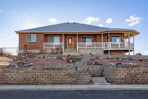 Single story home featuring covered porch, brick siding, and a shingled roof