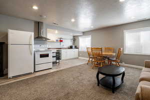 Kitchen with white appliances, a textured ceiling, recessed lighting, white cabinetry, and light colored carpet