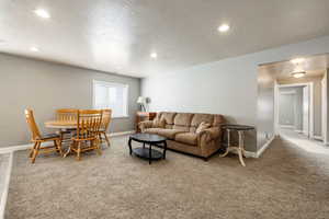 Living area with light carpet, a textured ceiling, and recessed lighting