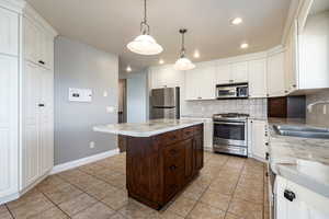 Two tone kitchen featuring stainless steel appliances, light tile patterned floors, pendant lighting, a center island, and decorative backsplash