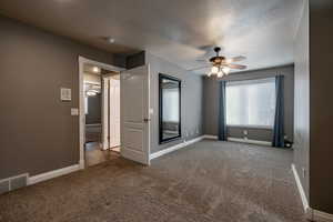 Unfurnished bedroom with a ceiling fan, dark carpet, and a textured ceiling