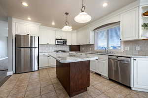 Kitchen with stainless steel appliances, white cabinetry, pendant lighting, a kitchen island, and light tile patterned floors