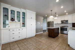 Two tone kitchen with stainless steel appliances, a center island, decorative light fixtures, dual tone cabinetry, and light tile patterned flooring