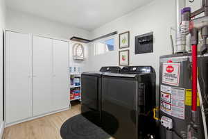 Laundry area with water heater, light wood-type flooring, and separate washer and dryer