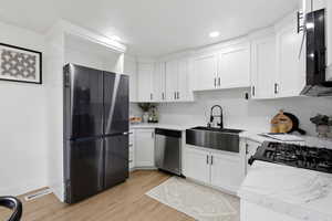 Kitchen featuring light countertops, appliances with stainless steel finishes, white cabinets, light wood-style floors, and decorative backsplash