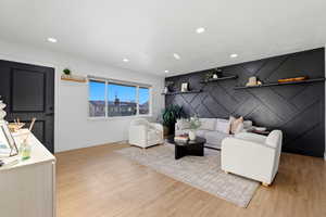 Living room with an accent wall, light wood-type flooring, and recessed lighting