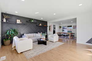 Living area with a decorative wall, light wood finished floors, an accent wall, and recessed lighting