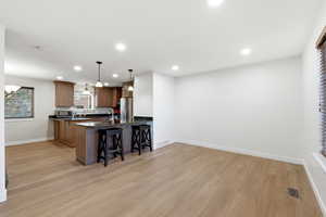 Kitchen featuring a kitchen breakfast bar, hanging light fixtures, brown cabinets, dark stone counters, and light wood finished floors