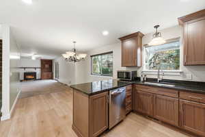 Kitchen with hanging light fixtures, a large fireplace, brown cabinets, dark stone counters, and healthy amount of natural light