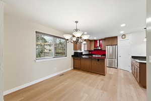 Kitchen featuring pendant lighting, a peninsula, stainless steel appliances, a chandelier, and wall chimney exhaust hood