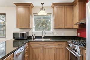 Kitchen with appliances with stainless steel finishes, dark stone counters, hanging light fixtures, extractor fan, and brown cabinets