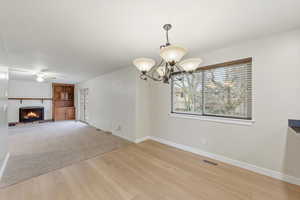 Unfurnished dining area featuring a large fireplace, light wood-style floors, light colored carpet, a chandelier, and ceiling fan