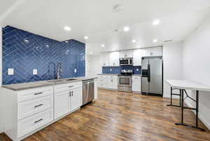 Kitchen featuring white cabinets, appliances with stainless steel finishes, dark wood finished floors, tasteful backsplash, and light stone countertops