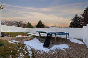 Yard layered in snow featuring a fenced backyard, a trampoline, a patio area, and an outdoor fire pit