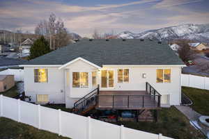 Rear view of house with a shingled roof, a fenced backyard, stucco siding, and a deck with mountain view