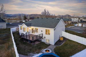 Back of house at dusk featuring a fire pit, roof with shingles, a deck with mountain view, a fenced backyard, and stucco siding