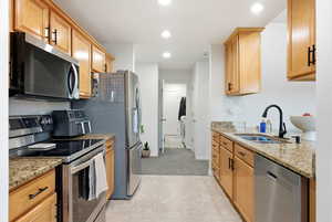 Kitchen with appliances with stainless steel finishes, light stone counters, recessed lighting, light tile patterned floors, and light colored carpet