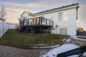 Back of property at dusk with a fenced backyard, a deck, stucco siding, an outdoor fire pit, and roof with shingles