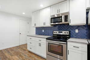 Kitchen featuring stainless steel appliances, white cabinets, dark wood-type flooring, recessed lighting, and backsplash