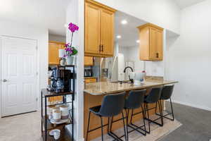 Kitchen featuring light stone counters, a breakfast bar area, stainless steel fridge, light brown cabinets, and a peninsula