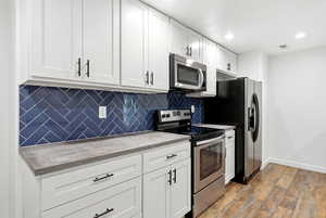 Kitchen featuring stainless steel appliances, white cabinetry, backsplash, dark wood finished floors, and recessed lighting