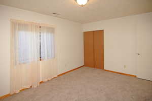 Unfurnished bedroom featuring a textured ceiling, a closet, and carpet