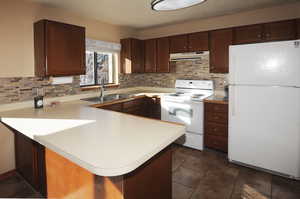 Kitchen featuring white appliances, a peninsula, light countertops, backsplash, and a textured ceiling