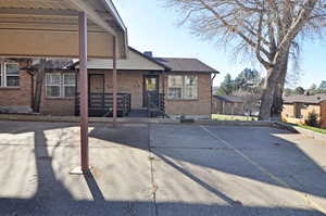 View of front of house with brick siding, a patio, uncovered parking, and a chimney