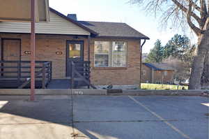 View of front facade with brick siding, uncovered parking, a chimney, and a shingled roof