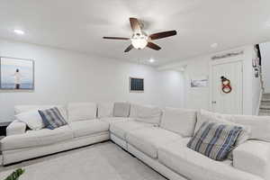 Carpeted living area with recessed lighting, ceiling fan, and stairway